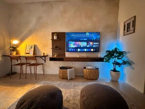 A living room with a TV, a desk, chairs, a potted plant, and a sofa. - Casa Oasis #4 - Cozy 1br apartment in lovely San Juan with AC and Solar Power (San Juan)