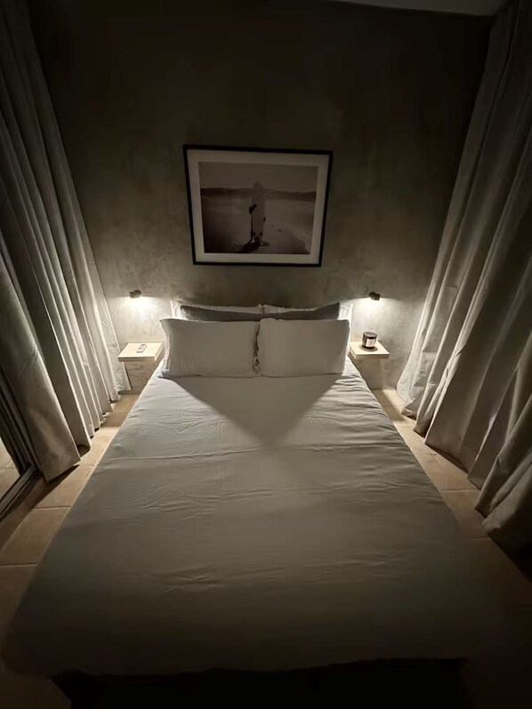 A neatly made bed with white linens, two bedside lamps, and a framed picture on the wall. - Casa Oasis #4 - Cozy 1br apartment in lovely San Juan with AC and Solar Power (San Juan)