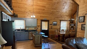 A cabin interior with a kitchen, dining area, and a leather sofa. - Tranquility Cabin: Secluded Mountain Escape with Game Room, Fire Pit & Hot Tub (Blue Ridge)