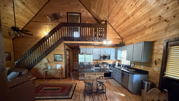 A spacious loft-style interior with a wooden ceiling, a staircase, a kitchen with modern appliances, and a dining area. - Tranquility Cabin: Secluded Mountain Escape with Game Room, Fire Pit & Hot Tub (Blue Ridge)