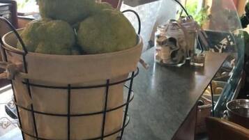 A kitchen counter with a wire basket containing green apples, a glass container with a plant, and a metal sink.