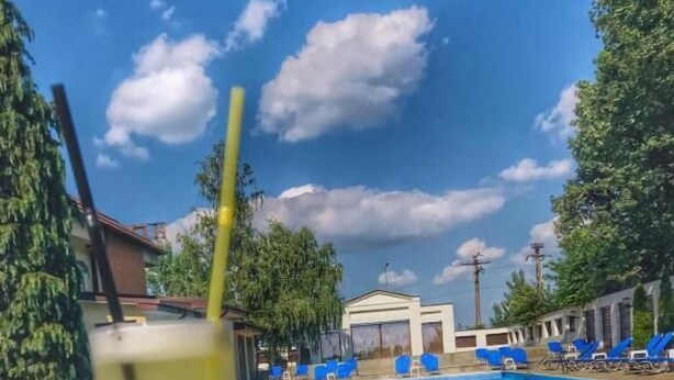 A swimming pool with lounge chairs, a glass of drink, and a building in the background. - Hotel President Scornicesti (Scornicesti)