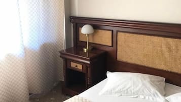 Une chambre d’hôtel avec un lit, une table de chevet avec une lampe, un tableau au mur et une fenêtre avec des rideaux.