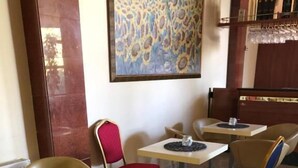 A hotel lobby with a row of tables and chairs, a large abstract painting on the wall, and a patterned carpet. - Hotel President Scornicesti (Scornicesti)