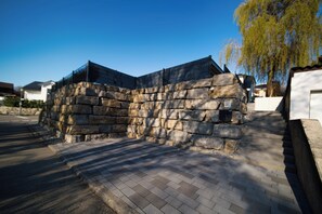 Un mur de pierres avec une clôture en métal, une zone pavée et un arbre.