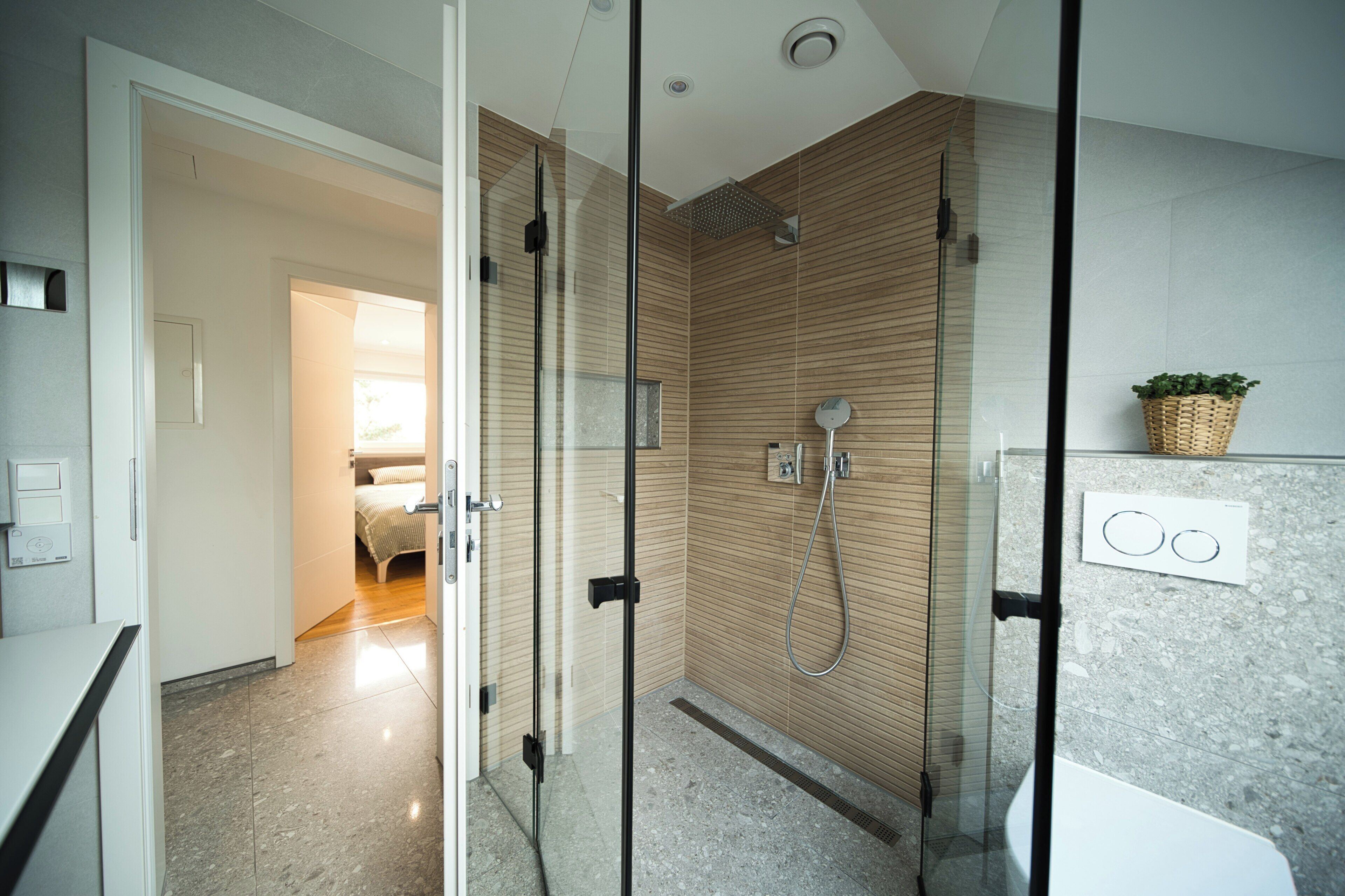Une salle de bain moderne avec une douche à parois de verre, un panneau mural en bois et un lavabo blanc.