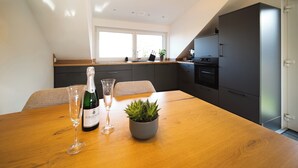 Een moderne keuken met een houten eettafel, een potplant, een fles wijn en een glas.