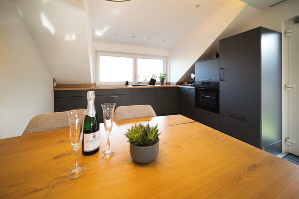 Une cuisine moderne avec une table à manger en bois, une plante en pot, une bouteille de vin et un verre.