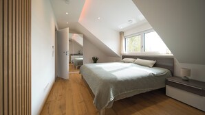 Een slaapkamer met een schuine plafond, een bed, een nachtkastje en een raam.