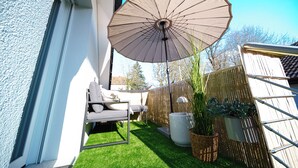 Een terras met een bank, een parasol en potplanten.