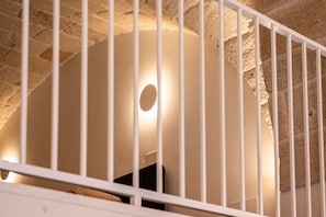 Ett rum med väggar av sten, ett runt fönster och ett vitt räcke.