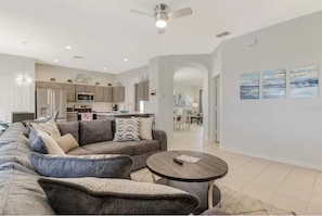 A modern living room with a sectional sofa, a round coffee table, and a dining area in the background. - Windsor Hills Lakefront •Walk to Waterpark •2mi WDW•6bd•No Rear Neighbors (Kissimmee)