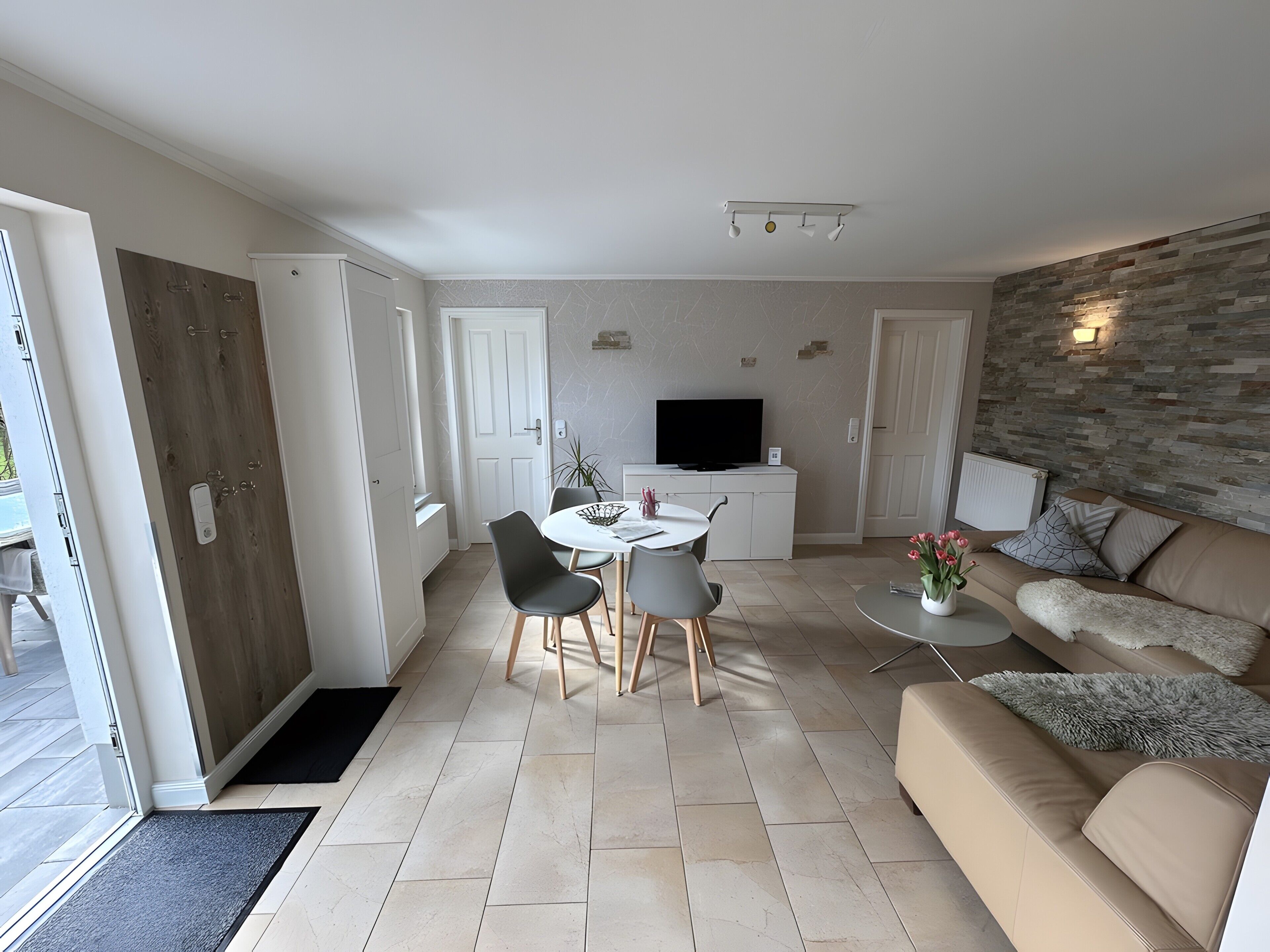 Una sala de estar moderna con un sofá, una mesa de comedor con sillas, un televisor y una pared de piedra.