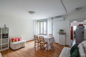 Een woonkamer met een eettafel, stoelen, een witte bank, een boekenkast en een radiator.
