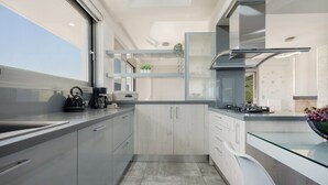 Ett modernt kök med ett stort fönster, vitvaror i rostfritt stål och en köksö i glas.