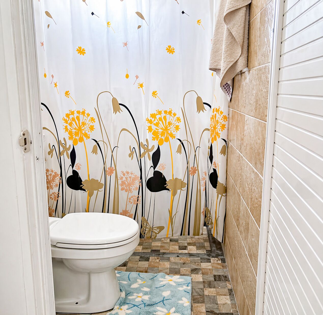 A bathroom with a toilet, patterned shower curtain, and tiled floor.