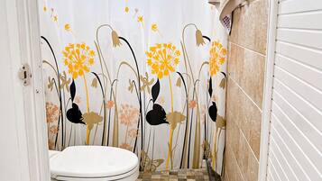 A bathroom with a toilet, patterned shower curtain, and tiled floor.