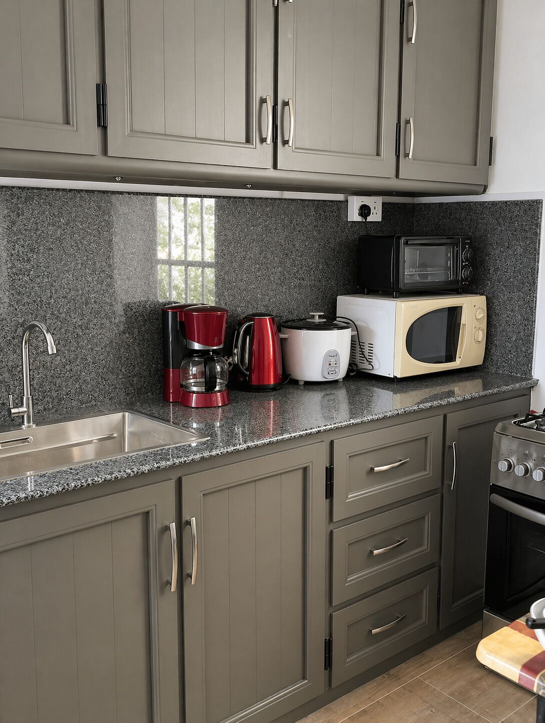 A kitchen with grey cabinets, a stainless steel sink, a microwave, a toaster, and a red coffee maker.