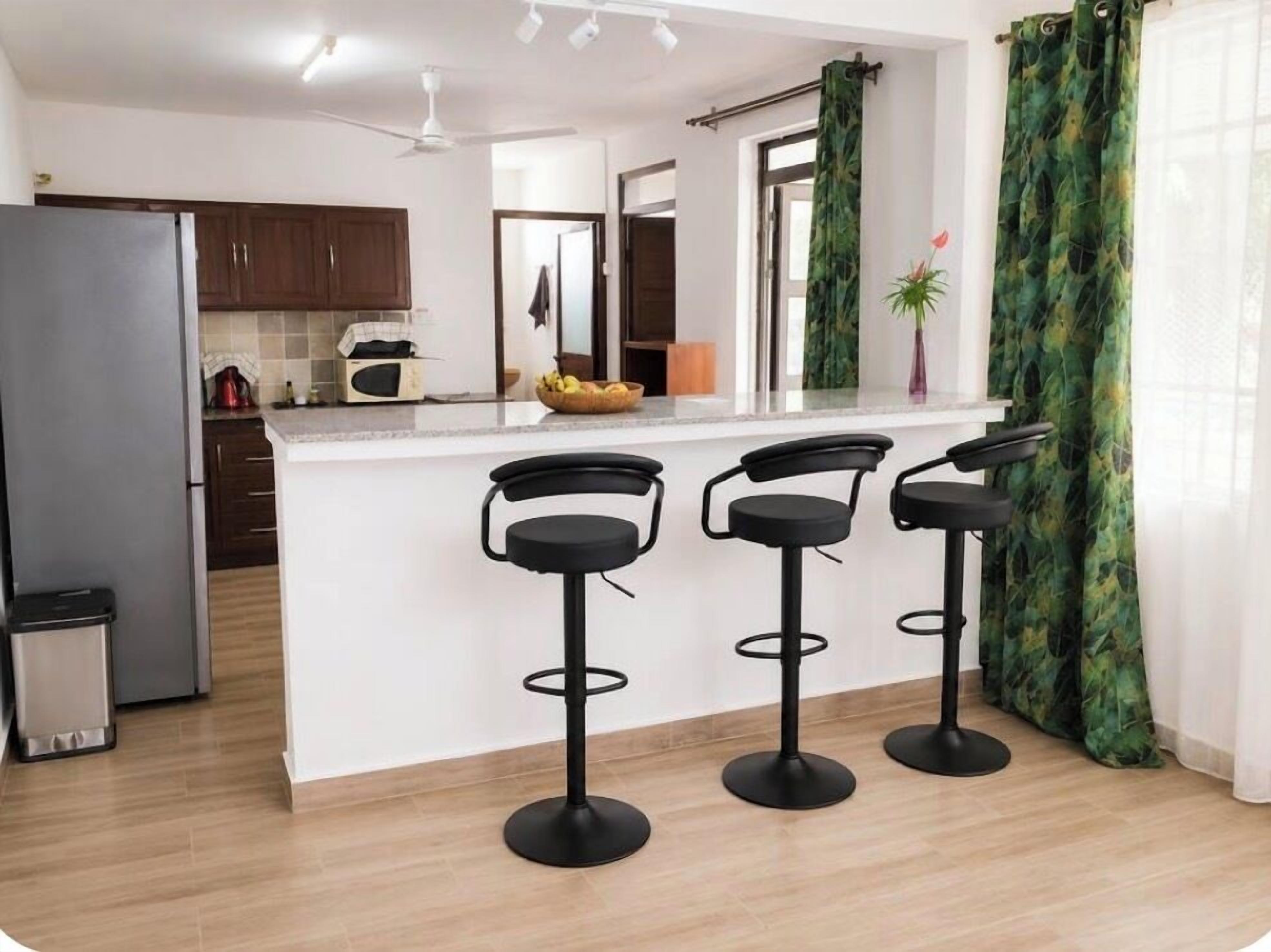 A modern kitchen with a central island, bar stools, a refrigerator, and a microwave.