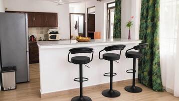 A modern kitchen with a central island, bar stools, a refrigerator, and a microwave.