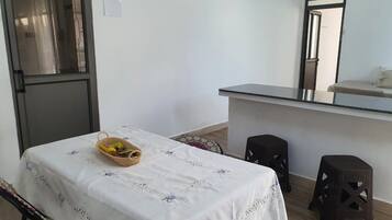 Une petite pièce propre, avec un lit, une table sur laquelle se trouve un panier, et un coin cuisine.
