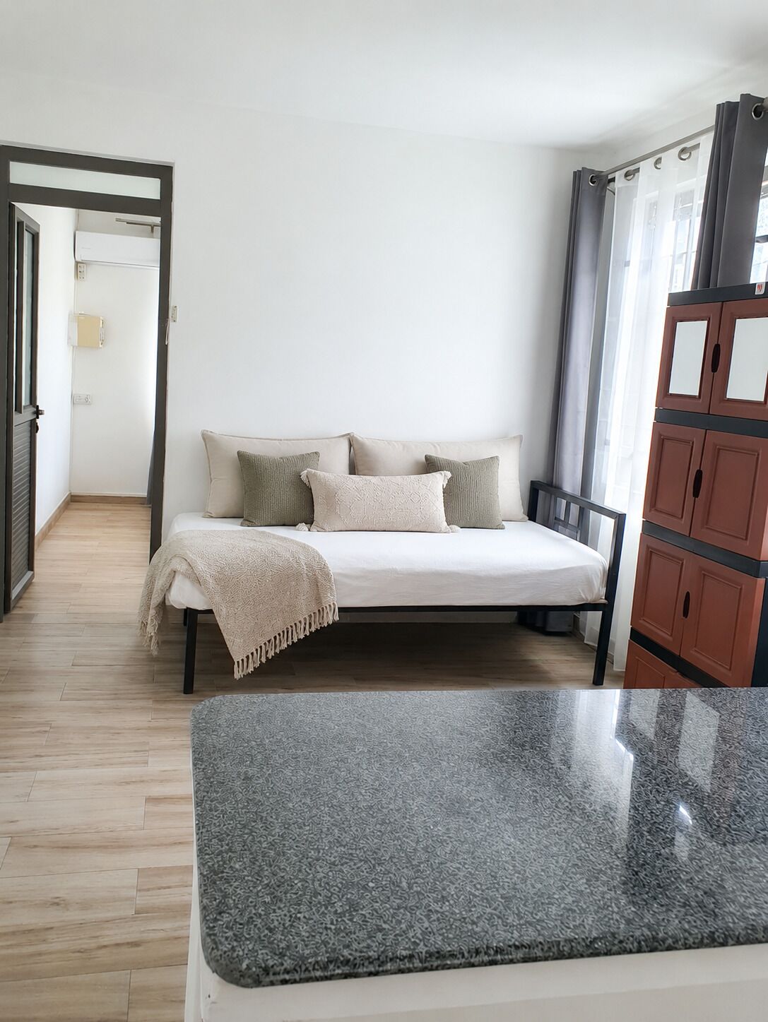 A bedroom with a bed, a grey rug, a wardrobe, and a door leading to another room.