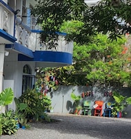 A building with a blue and white facade, a balcony, and a garden area with potted plants and outdoor furniture.