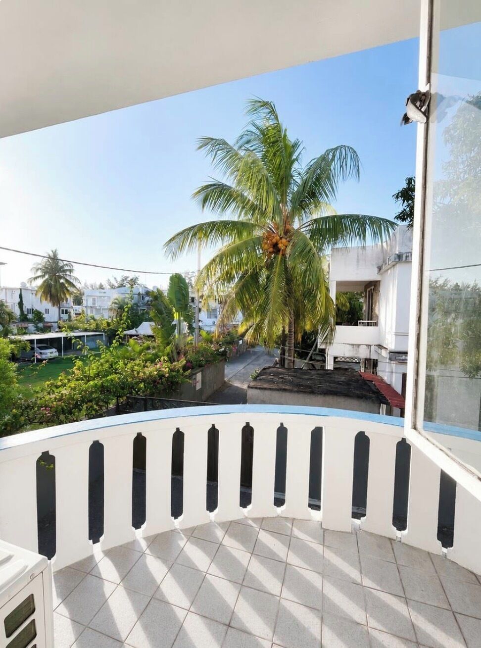 Un balcon donnant sur un quartier résidentiel, avec vue sur des palmiers et des maisons.