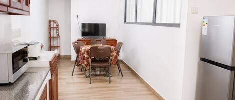 Una cocina compacta con una mesa de comedor, sillas, un refrigerador y una televisión.