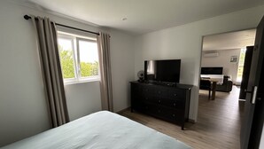 Un dormitorio con cama, cómoda, televisor y ventana con cortinas.