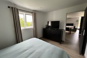 Ein Schlafzimmer mit Bett, Schminktisch, Fernseher und einem Fenster mit Vorhängen.