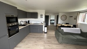 Una cocina moderna con electrodomésticos integrados, un comedor con mesa y sillas, un sofá y un reloj en la pared.
