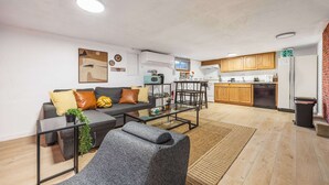 A modern living room with a sofa, coffee table, and a kitchen area with wooden cabinets and appliances. - Modern 2BR Basement • Near LRT • Parking (Seattle)