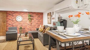 A living room with a brick wall, a sofa, a coffee table, and a dining area with a table set for two. - Modern 2BR Basement • Near LRT • Parking (Seattle)
