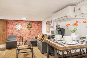 Ein Wohnzimmer mit Backsteinwand, einer Couch, einem Couchtisch und einem Essbereich mit Tisch für zwei Personen.