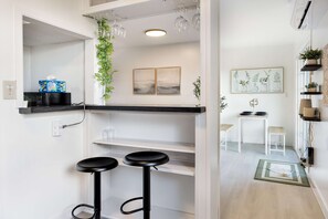 Una cocina moderna con taburetes negros, microondas, cafetera y una planta colgante.