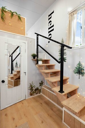 Eine Treppe mit Holzhäuschen und schwarzen Geländern, eine weiße Tür und eine Wand mit einem 'hello' Schild.