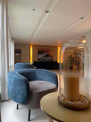 Eine moderne Lobby mit einem blauen Sessel, einer Glaskuppel über einem Teelicht und einem großen abstrakten Gemälde an der Wand.