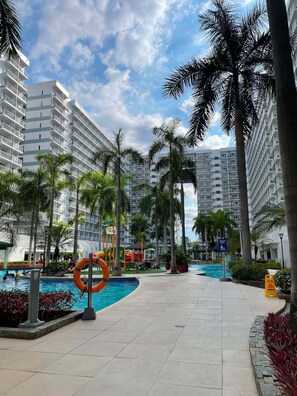 A resort with a swimming pool, palm trees, and high-rise buildings in the background. - Shell Residences MOA - The Executive Suites SL005 Cozy 1 Bedroom with AC, Wi-Fi (Pasay City)