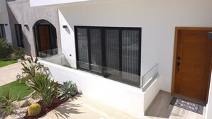 Ein modernes Gebäude mit einem Glasbalkon, einer Holztür und einem kleinen Garten mit Kakteen und Sukkulenten.