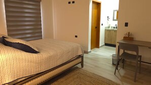 Ein Schlafzimmer mit Bett, Schreibtisch und Blick auf eine Küche.