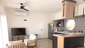 Eine moderne Küche mit Kochinsel, Backofen und Kühlschrank. Ein Flachbildfernseher steht auf einem Lowboard, ein Deckenventilator ist installiert, und die Spritzschutzwand ist mit einem Muster versehen.
