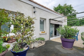 Un bâtiment à l’extérieur blanc, avec une porte et une fenêtre. On y trouve des plantes en pot et une enseigne sur laquelle est écrit « Bienvenue ».