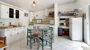 A kitchen with white cabinets, a dining table with chairs, a hanging light fixture, and a microwave. - Independent House 5 Minutes from the Beaches (Les Mathes)