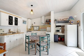 Une cuisine avec des meubles blancs, une table à manger avec des chaises, un luminaire suspendu et un four à micro-ondes.