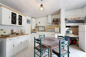 A kitchen with white cabinets, a wooden dining table, and teal chairs. - Independent House 5 Minutes from the Beaches (Les Mathes)