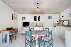 A dining area with a round table, chairs, a television, cabinets, and a ceiling light fixture. - Independent House 5 Minutes from the Beaches (Les Mathes)
