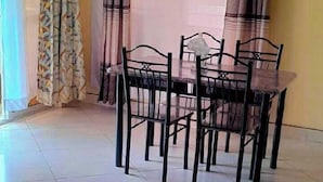 A dining area with a table and chairs, a window with curtains, and a tiled floor. - Lux Suites Concord Apartments Mtwapa (Mtwapa)
