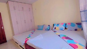 A bedroom with a bed, a ceiling fan, a wardrobe, and a door. - Lux Suites Concord Apartments Mtwapa (Mtwapa)