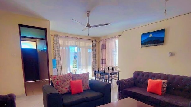 A living room with two sofas, a coffee table, a dining table, and a ceiling fan. - Lux Suites Concord Apartments Mtwapa (Mtwapa)